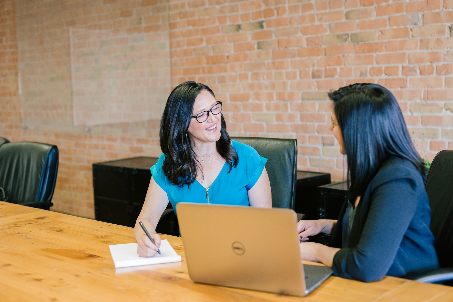 woman-in-teal-t-shirt-sitting-beside-woman-in-suit-jacket-in-a-meeting-room-at-Al-Zahronix-Consulting